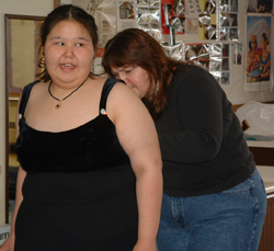 A women helping a young girl fit properly into her dress with a few quick stitches.